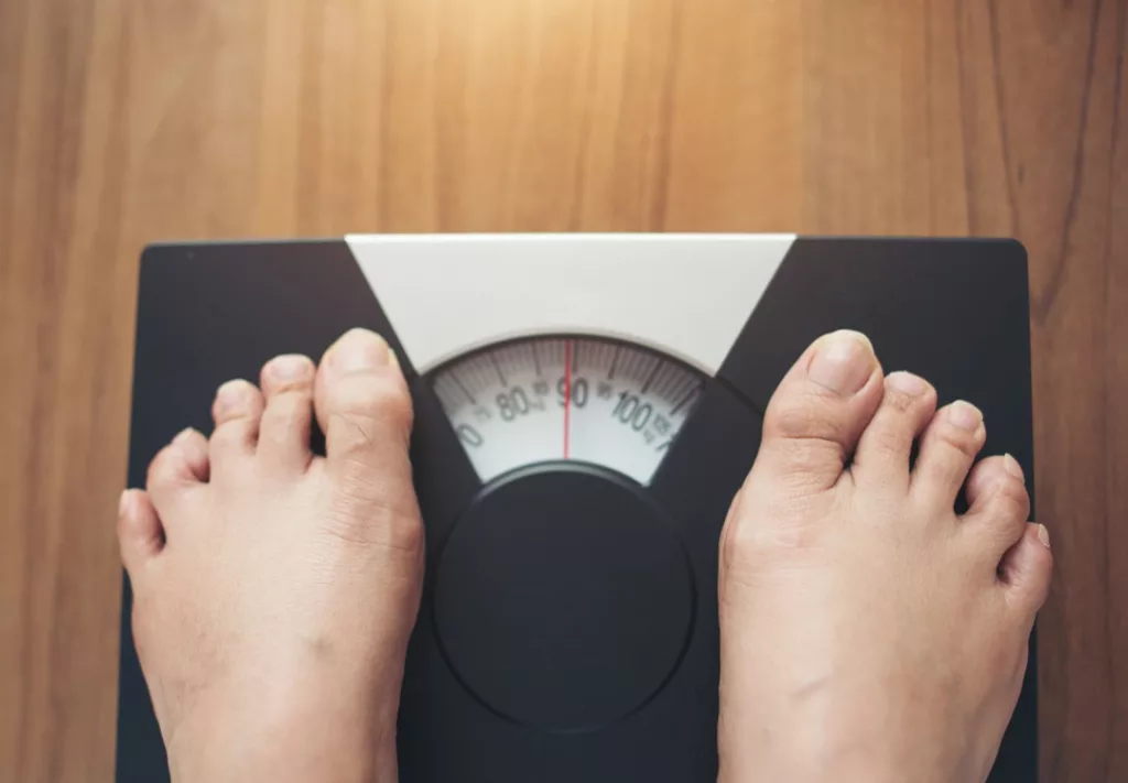 Obesity, woman-feet standing weight scale wooden background